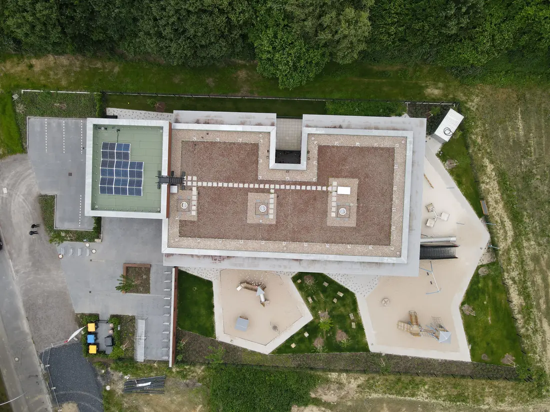 Luftaufnahme eines Neubaus mit umlaufenden Außenanlagen, Parkplatz und Spielflächen