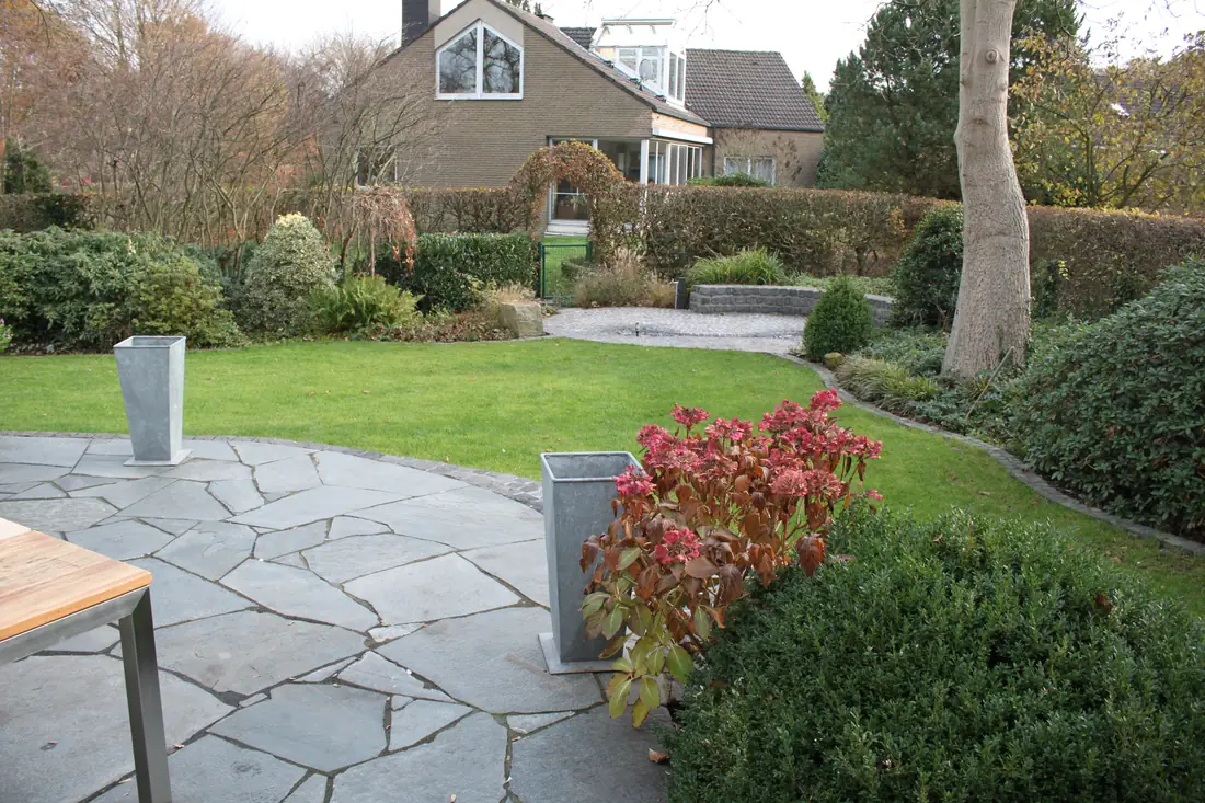 Terrasse aus Polygonalplatten mit angrenzendem Rasen und Bepflanzung