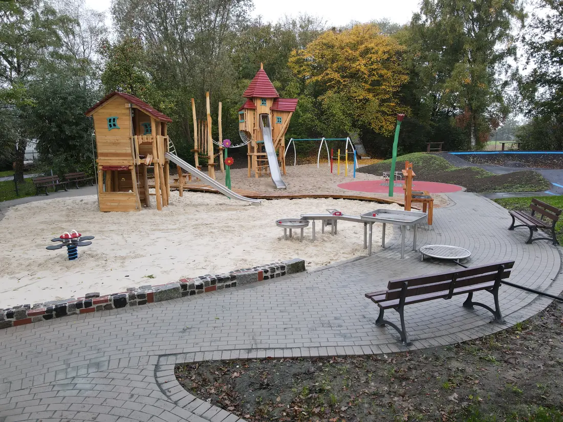 Spielplatz mit Holzspielturm, Rutsche und Sandfläche vor Herbstbäumen